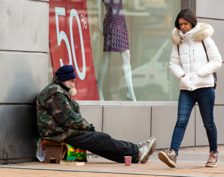 Sofia, Bulgaria - 22 January 2019: Young woman passes homeless elderly man who begs for money in front of a clothing store at Vitosha Boulevard in Sofia.のeditorial素材
