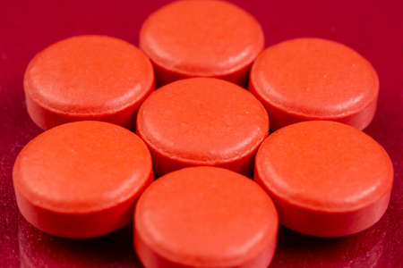 Red pills isolated on a red reflective background. Global pharmaceutical industry for billions dollars per year. Pharmaceutical drugs for use as medications. Studio shot.の写真素材