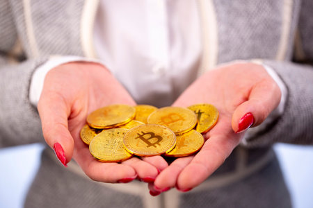 Virtual cryptocurrency money Bitcoin golden coins in the hands of a woman with red nail polish. The...