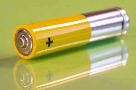 Single AAA battery is seen on a reflective green surface. Closeup view from the plus side of the...