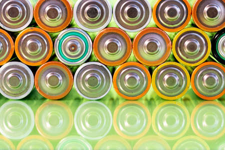 Multiple used AA alkaline batteries are seen arranged in a pile on a reflective green surface. Closeup front view from the plus side of the battery.の写真素材