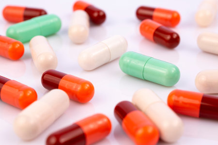 Colorful capsules and pills isolated on white reflective background. Global pharmaceutical industry...