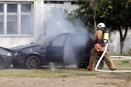 Firefighters participate in a training where they extinguish fire from a car crashed into another...