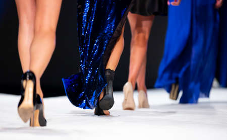 Female models walk the runway in beautiful designer dresses during a Fashion Show. Fashion catwalk event showing new collection of clothes. Unrecognizable people. High heels shoes. Legs from the back.の写真素材