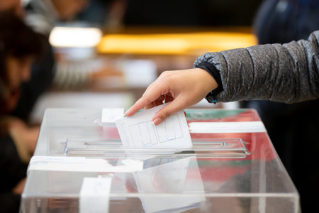 A woman casts her envelope vote into a transparent plastic ballot box. Human hand voting.