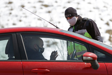 Sofia, Bulgaria - 3 April, 2020: A police officer checks a car drriver at one of the exits of Sofia, following restrictions on non-essential travel between cities and towns due to coronavirus disease.のeditorial素材
