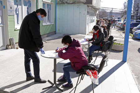 Sofia, Bulgaria - April 8, 2020: People wearing face masks in an attempt to prevent the spread of coronavirus disease COVID-19 wait in line in front of an office of the labor bureau.のeditorial素材