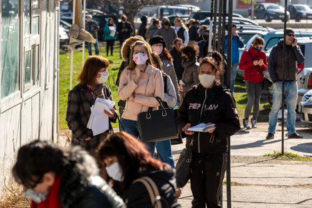 Sofia, Bulgaria - April 8, 2020: People wearing face masks in an attempt to prevent the spread of coronavirus disease COVID-19 wait in line in front of an office of the labor bureau.のeditorial素材