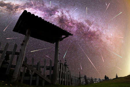 A view of a Meteor Shower and the purple Milky Way with wooden entrance door with a roof and fence silhouette in the foreground. Night sky nature summer landscape. Perseid Meteor Shower observation. Colorful shooting stars.の写真素材