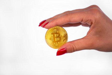 Virtual cryptocurrency money Bitcoin golden coin in the right hand of a woman with red nail polish....
