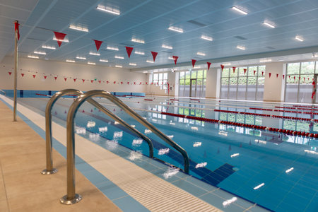 Indoor swimming pool full of water with ladder on the side.のeditorial素材