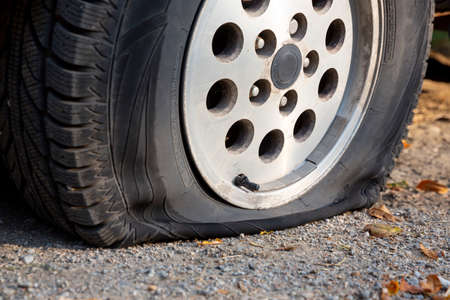 A car with a flat tire is seen parked on a dirt road.の写真素材