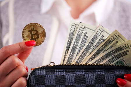 Virtual cryptocurrency money Bitcoin golden coins in the left hand of a woman with red nail polish and a purse. The future of money. US dollars.の写真素材