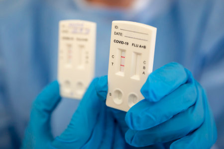 Positive COVID-19 rapid test is seen in the hand of a medical worker wearing personal protective equipment.の写真素材