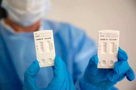 Positive COVID-19 rapid test is seen in the hand of a medical worker wearing personal protective equipment.の写真素材
