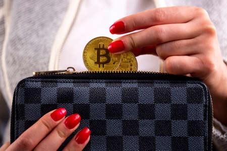 Virtual cryptocurrency money Bitcoin golden coins in the left hand of a woman with red nail polish and a purse. The future of money.の写真素材