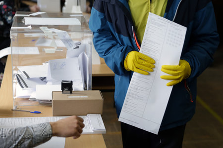 Sofia, Bulgaria: 4 April, 2021: Person with protective gloves receives his ballot at a polling station during the parliamentary elections.のeditorial素材