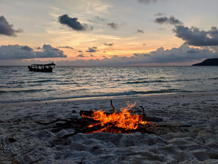 Bonfire at the beach with sunset and boat in the back