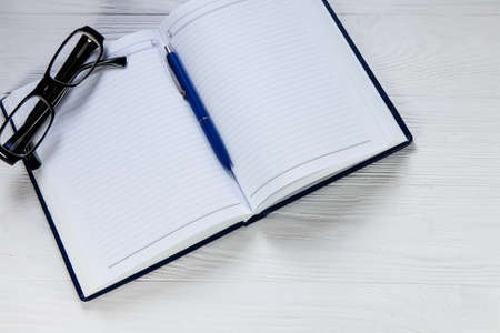 Blank notebook with pen and eyeglasses on wooden tableの写真素材