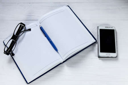 Blank notebook with pen. eyeglasses and mobile phone on wooden tableの写真素材