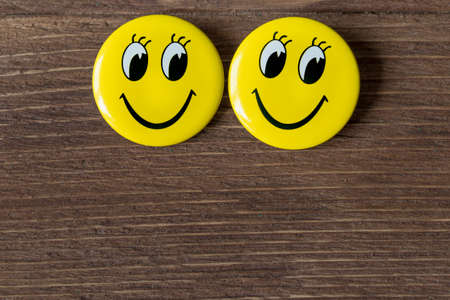 Two yellow buttons with smiley faces on a wooden backgroundの写真素材