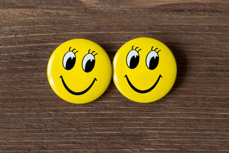 Two yellow buttons with smiley faces on a wooden background.の写真素材