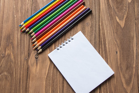 Colored pencils on top and notepad on wooden background