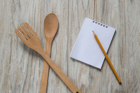 Wooden spoon and spatula with notebook and pencil on wooden backgroundの写真素材