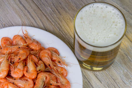 heap of boiled shrimps in white plate and glass of beer on wooden surface, close-upの写真素材
