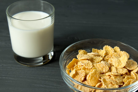 Corn flakes on glass bowl and glass of milk isolated on grey surface, closeup