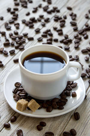 Black coffe in a white cup and cane sugar on a plate on wooden background, close-upの写真素材