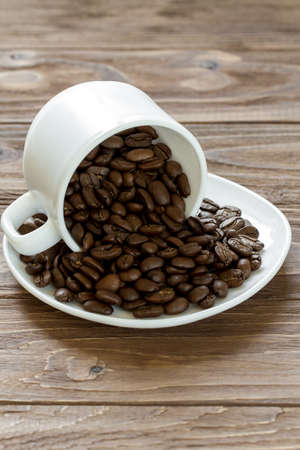 Roasted coffee beans spilled of a cup on a plate on wooden background, closeupの写真素材