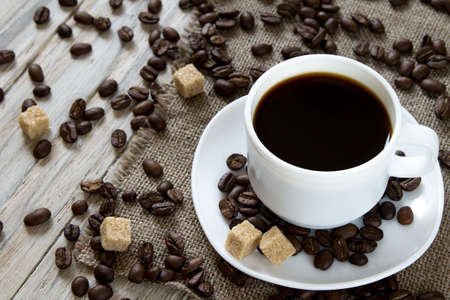 Black coffee in a mug and scattered roasted beans on wooden background, top viewの写真素材