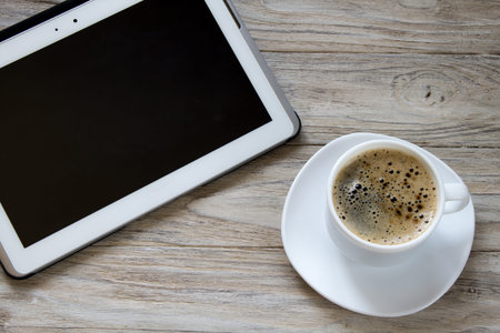 Cup of coffee and tablet on wooden background, top viewの写真素材