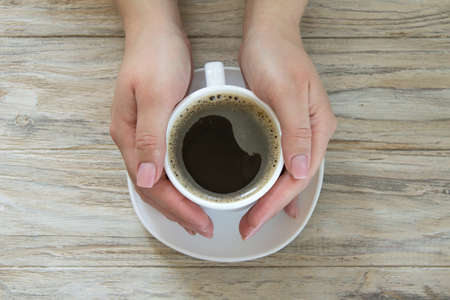 Cup of black aroma coffee in womans hand on wooden background, top viewの写真素材
