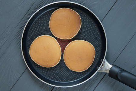 Pancakes in a frying pan on wooden surfaceの写真素材