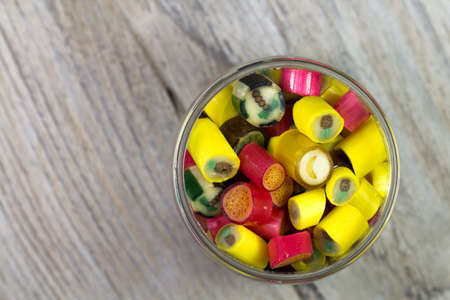 Many sweet colorful candies in opened glass jar on wooden background, top viewの写真素材