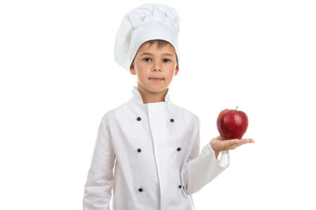 Talented cute boy in white chef uniform holding red apple on white backgroundの写真素材