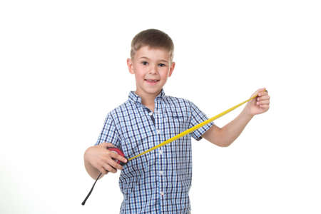 Small handsome builder boy dressed in blue checkered shirt holds a measuring tape, isolated on white background.の写真素材