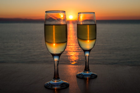 Romantic evening, sunset, two wineglasses, sun path on the water between two wineglasses with wine.