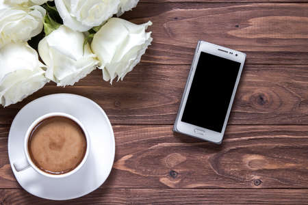 Wooden surface with bouquet of roses, cup of coffee and phone. Romantic wallpaper for a desktopの写真素材