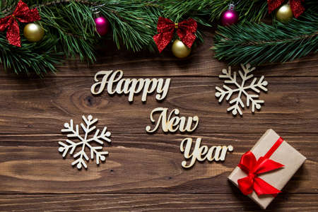 Happy New Year with two beautiful snowflakes and a gift box on the center of the wooden background with pine tree branches on the top of the screenの写真素材