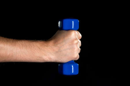 Health is your wealth. Male hand holding the blue dumbbell on the black backgroundの写真素材