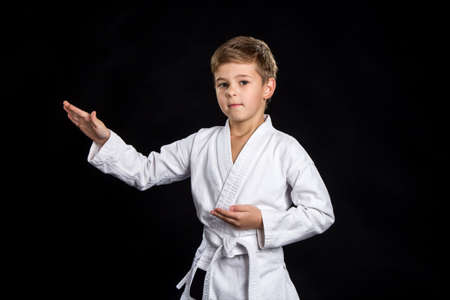 Macro with male fighter in kimono shows pose with open palms. Serious kid in brand new kimono on the black backgroundの写真素材