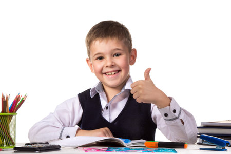 Cheerful satisfied pupil sitting at the desk with thumb up surrounded with stationery