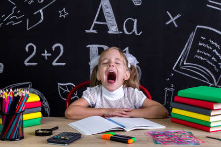 Yawning girl sitting at the desk with books, school suppliesの写真素材