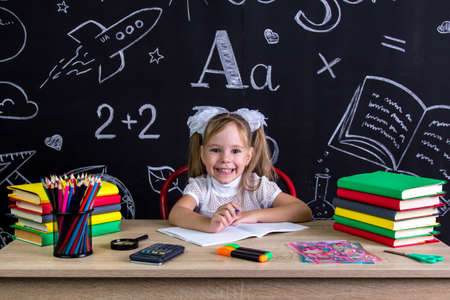 Excited schoolgirl sitting at the desk with books, school supplies, holding the pen in the right handの写真素材