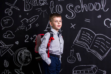 Happy schoolboy standing before the chalkboard as a background with a backpack on his back. Landscape pictureの写真素材