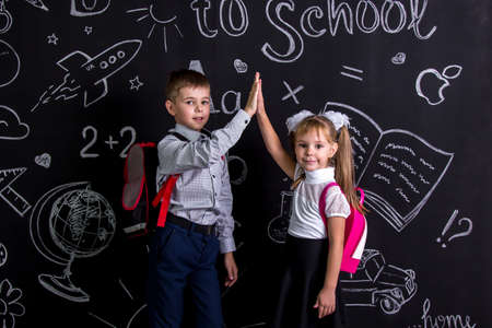 Boy and girl. School mates standing before the chalkboard as a background with a backpack on their backs claping their hands looking straight to the cameraの写真素材
