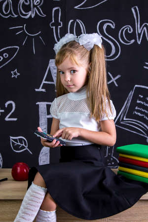Puzzled schoolgirl sitting on the desk with books, school supplies, doing maths with calculator looking at the camera.の写真素材